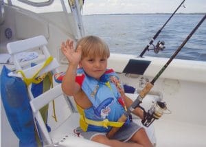 young boy fishing and waving at camera